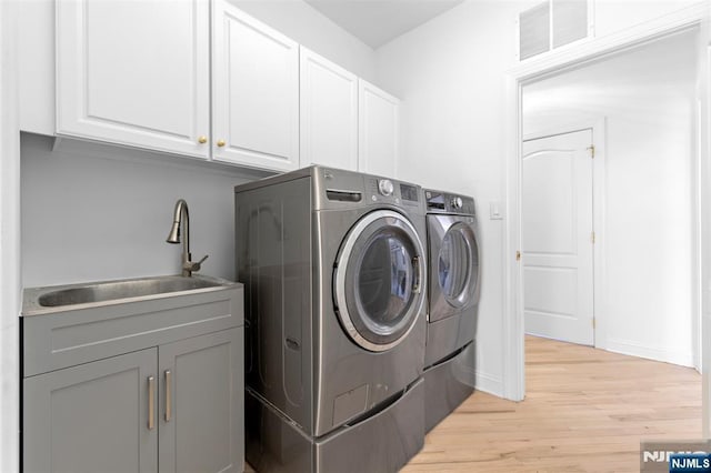laundry area with washing machine and clothes dryer, a sink, light wood finished floors, visible vents, and cabinet space