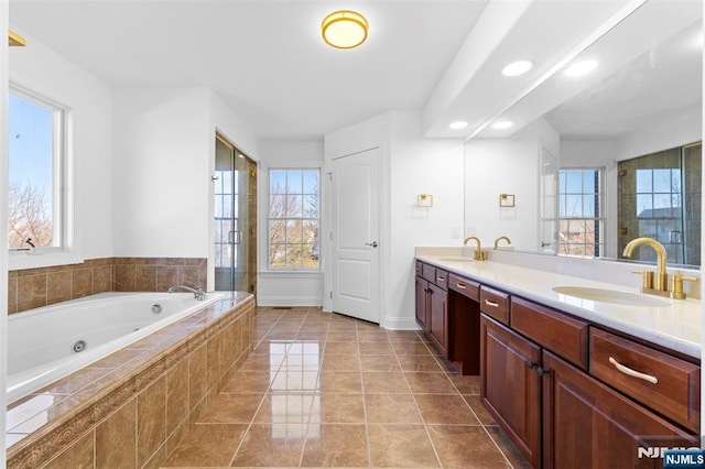full bathroom with plenty of natural light, double vanity, a tub with jets, and a sink