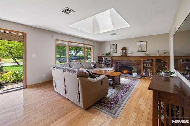 living room featuring a brick fireplace, a skylight, visible vents, and light wood-style floors