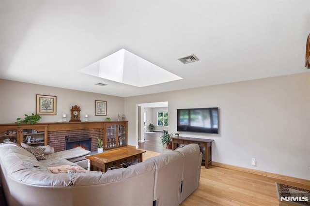 living room with visible vents, a brick fireplace, baseboards, light wood-style flooring, and a skylight