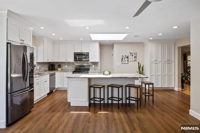 kitchen featuring white cabinets, a skylight, appliances with stainless steel finishes, and dark wood-type flooring