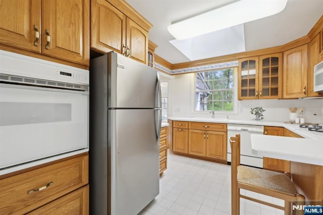 kitchen featuring light tile patterned floors, a sink, light countertops, glass insert cabinets, and white appliances