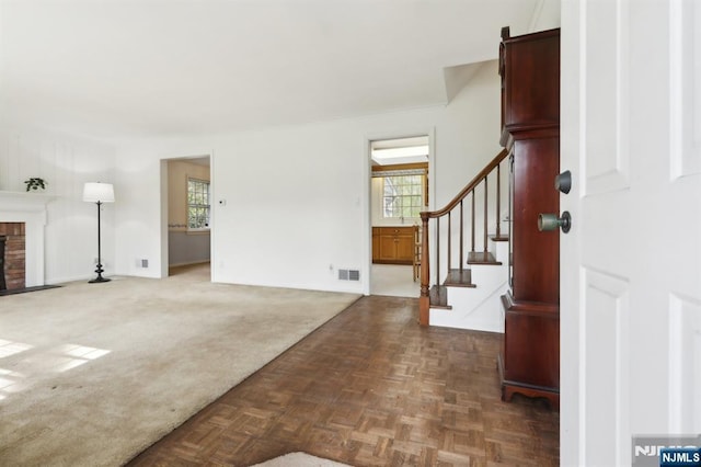 foyer entrance featuring visible vents, a brick fireplace, and stairway