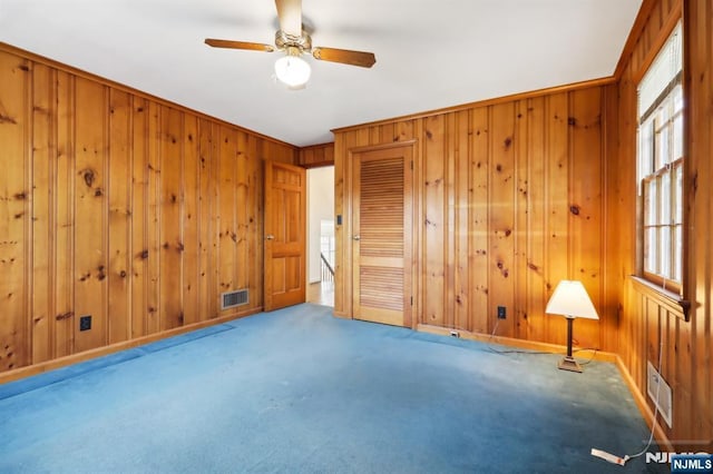 carpeted spare room featuring visible vents, wood walls, and a healthy amount of sunlight
