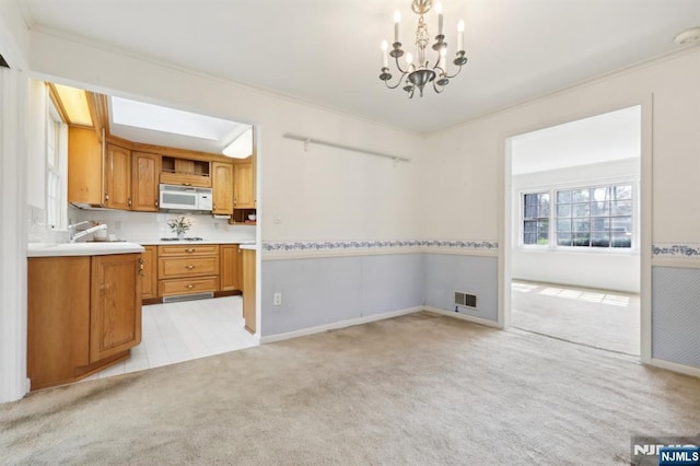 unfurnished dining area featuring visible vents, crown molding, a chandelier, and light colored carpet
