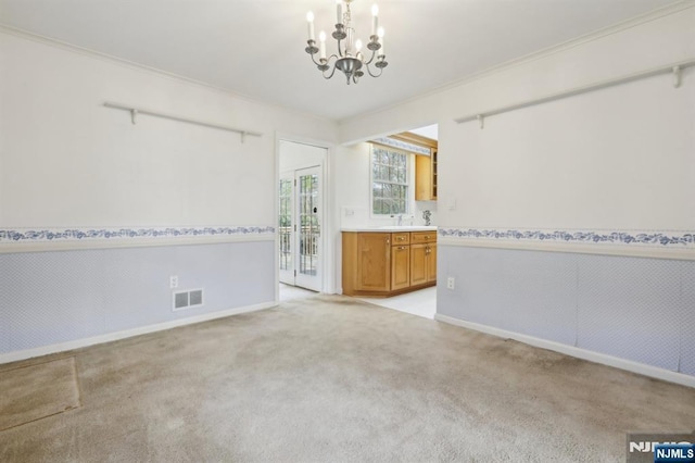 unfurnished room with visible vents, a wainscoted wall, baseboards, a notable chandelier, and light carpet