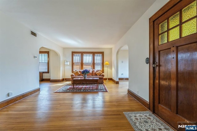 foyer featuring baseboards, visible vents, arched walkways, and wood-type flooring