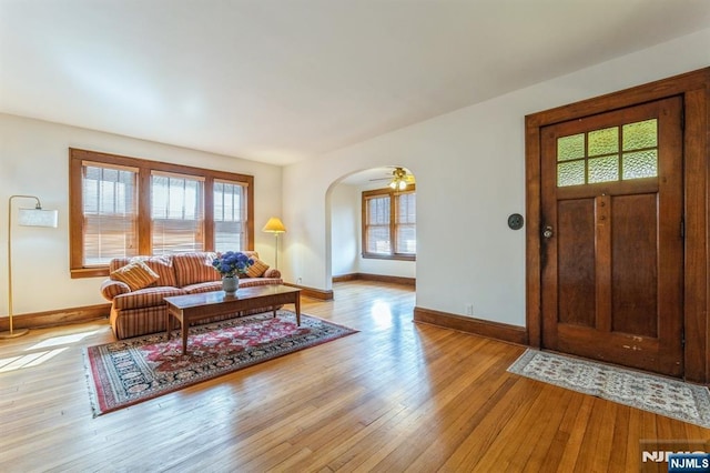entrance foyer with light wood finished floors, arched walkways, a wealth of natural light, and baseboards
