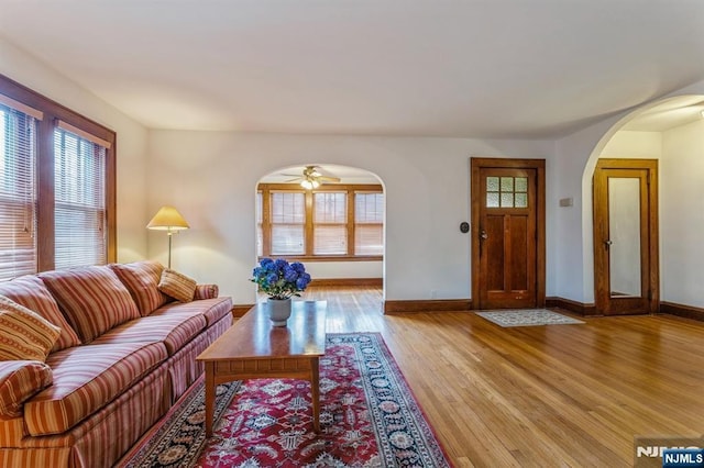 living room featuring baseboards, arched walkways, ceiling fan, and light wood-style floors