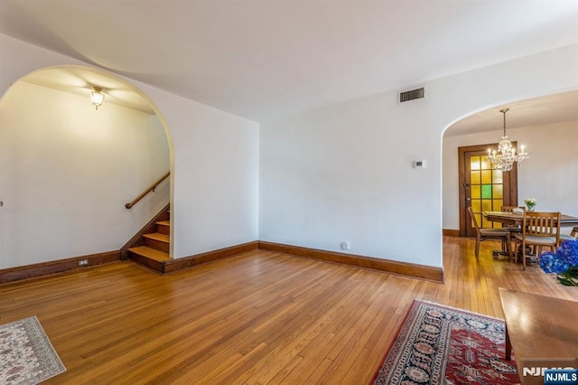 unfurnished living room with visible vents, hardwood / wood-style floors, baseboards, arched walkways, and a notable chandelier