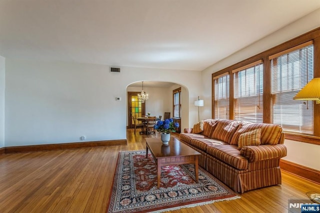 living room featuring a chandelier, visible vents, hardwood / wood-style floors, baseboards, and arched walkways