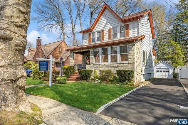 view of front of house with driveway, an outdoor structure, a front lawn, and stone siding