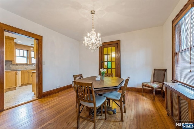 dining area with light wood-type flooring, a notable chandelier, and baseboards