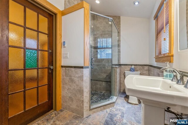 full bathroom with a shower stall, stone finish flooring, a wainscoted wall, recessed lighting, and tile walls