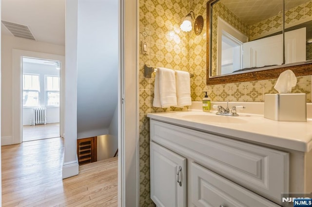 bathroom with radiator, vanity, visible vents, baseboards, and wood finished floors