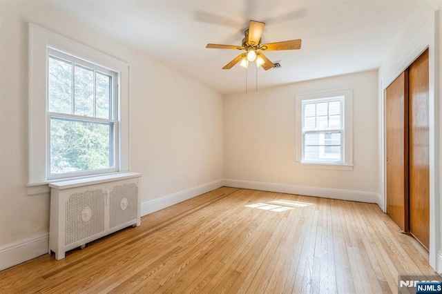 unfurnished bedroom with light wood-style floors, a closet, radiator heating unit, baseboards, and visible vents