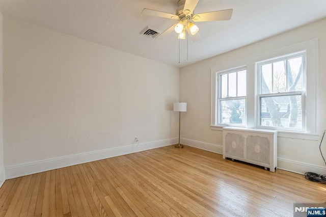 unfurnished room with baseboards, visible vents, radiator, and light wood-type flooring