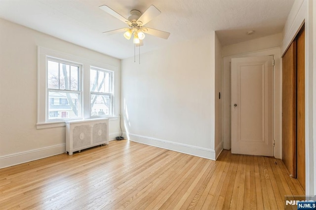 unfurnished room with baseboards, light wood-type flooring, radiator, and a ceiling fan