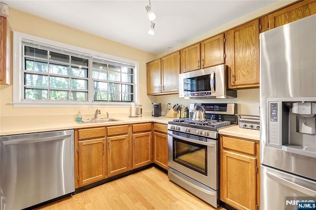 kitchen featuring brown cabinetry, light countertops, a sink, light wood finished floors, and appliances with stainless steel finishes