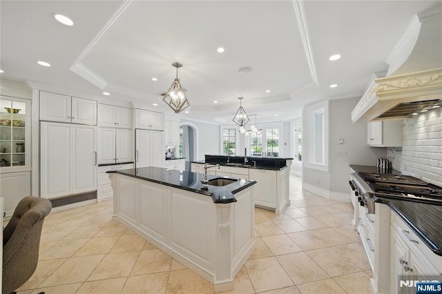 kitchen featuring dark countertops, a sink, a center island with sink, and a raised ceiling