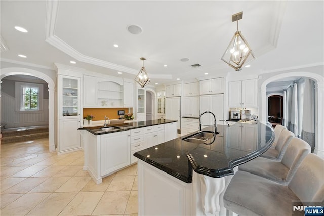 kitchen with dark countertops, open shelves, a sink, a large island, and arched walkways