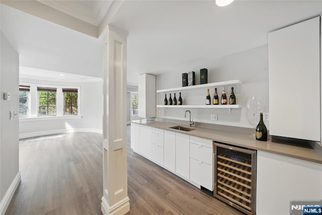 bar featuring beverage cooler, wet bar, wood finished floors, ornamental molding, and a sink
