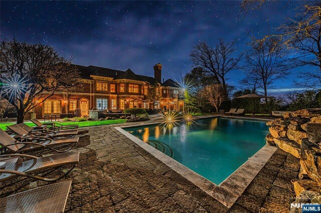 pool at twilight with a patio area and an outdoor pool