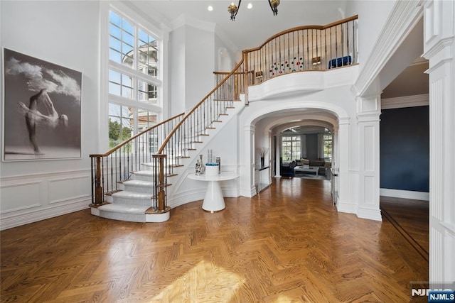 entrance foyer with stairway, a high ceiling, ornamental molding, arched walkways, and decorative columns