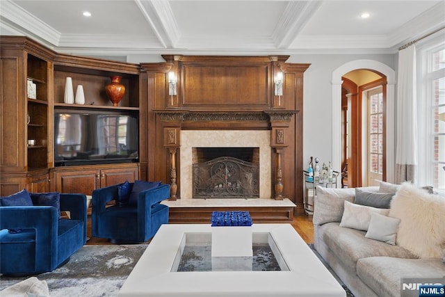 living area featuring crown molding, wood finished floors, arched walkways, a fireplace, and beam ceiling