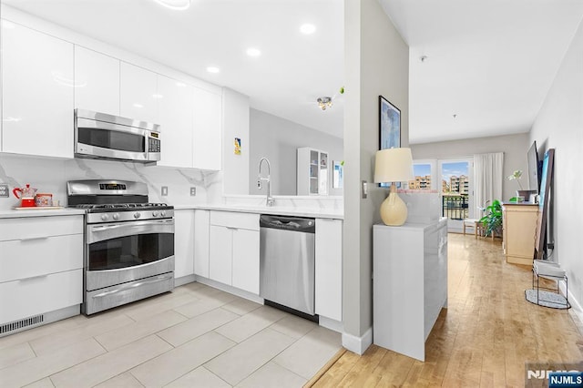 kitchen featuring modern cabinets, white cabinets, light countertops, stainless steel appliances, and backsplash