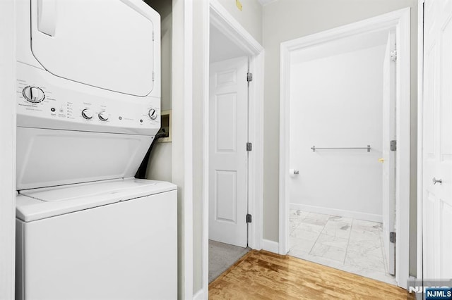 clothes washing area with baseboards, stacked washer and clothes dryer, marble finish floor, and laundry area