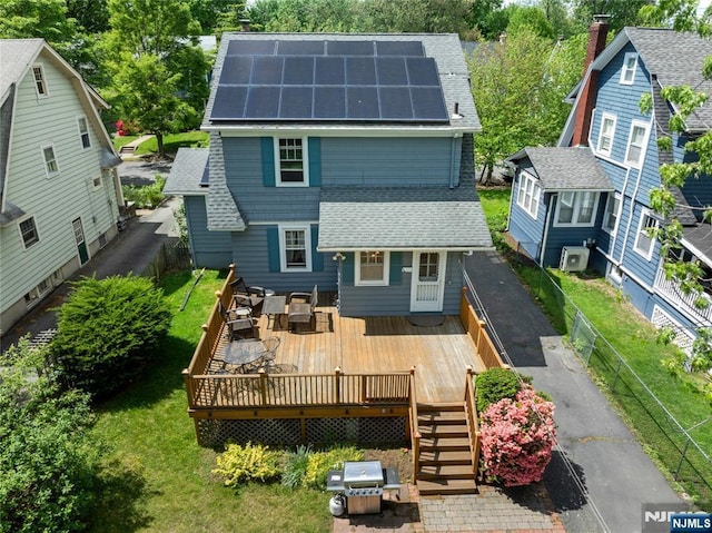 rear view of property featuring a shingled roof, a wooden deck, roof mounted solar panels, central AC, and stairway