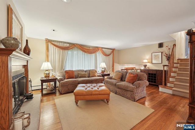 living area with wood-type flooring, stairway, a fireplace, and baseboard heating