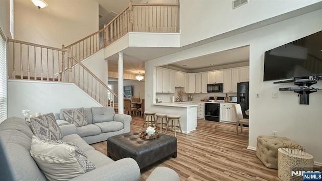 living area with a towering ceiling, light wood-type flooring, stairway, visible vents, and decorative columns