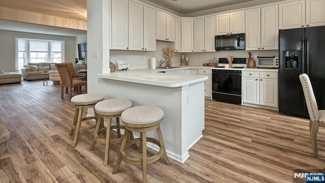 kitchen featuring a sink, a kitchen breakfast bar, light wood-type flooring, and black appliances