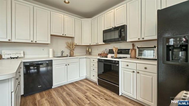 kitchen featuring light countertops, light wood-style floors, a sink, and black appliances