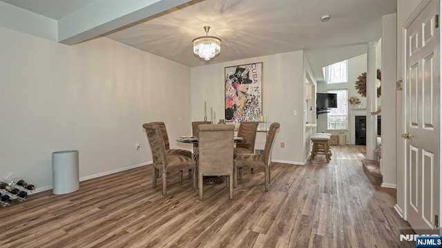 dining room with wood finished floors, a notable chandelier, a glass covered fireplace, and baseboards