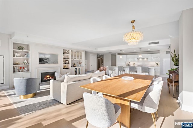 dining area with an inviting chandelier, a tray ceiling, light wood-type flooring, visible vents, and a high end fireplace