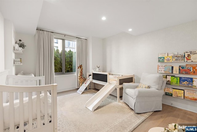 bedroom with wood finished floors, a crib, baseboards, and recessed lighting
