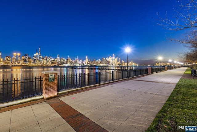 exterior space with a water view, fence, and a view of city lights