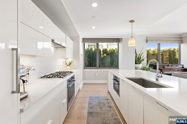 kitchen featuring tasteful backsplash, white cabinets, light wood-style floors, stainless steel appliances, and a sink