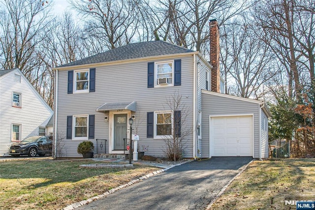 colonial house featuring an attached garage, a chimney, aphalt driveway, and a front yard