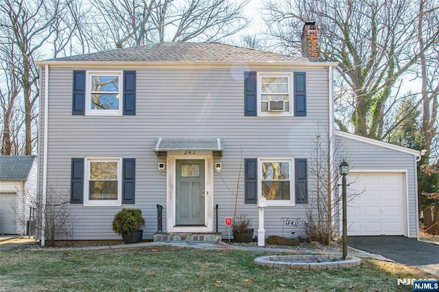 colonial-style house featuring an attached garage, a chimney, aphalt driveway, and a front yard