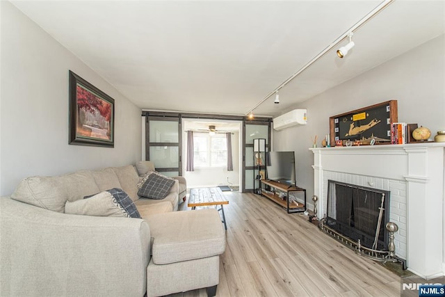 living room with a brick fireplace, light wood-style floors, an AC wall unit, and track lighting