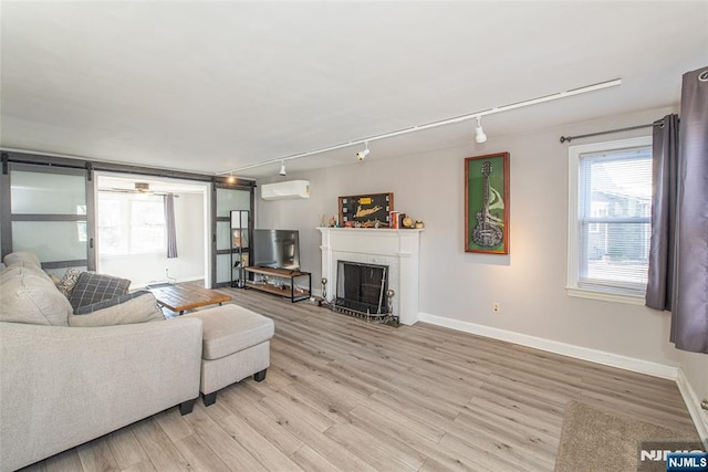 living area with light wood-style flooring, a wall mounted AC, plenty of natural light, and a brick fireplace