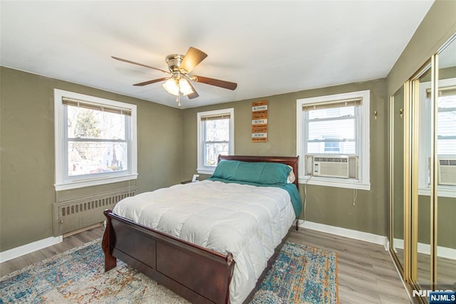 bedroom with light wood-type flooring, baseboards, cooling unit, a ceiling fan, and radiator