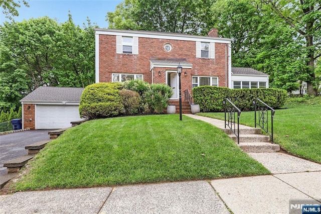 view of front of home with brick siding, a chimney, a front lawn, and asphalt driveway