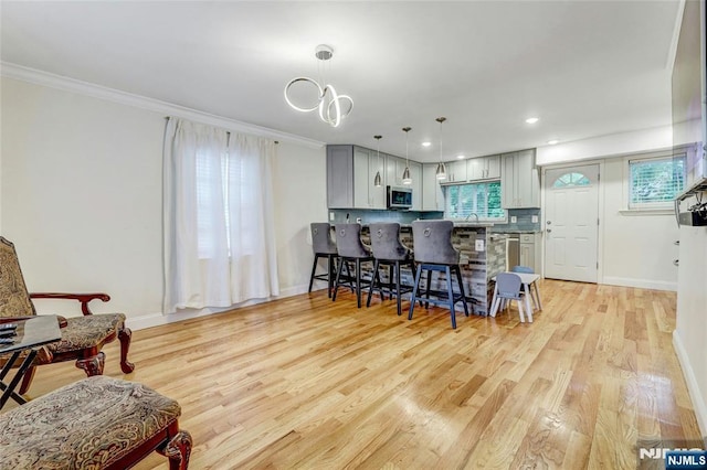 kitchen featuring stainless steel microwave, a kitchen breakfast bar, ornamental molding, gray cabinetry, and light wood finished floors