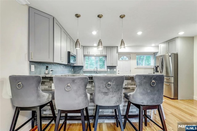 kitchen with stainless steel appliances, gray cabinets, a breakfast bar, and tasteful backsplash