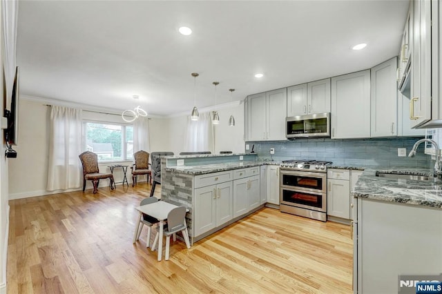 kitchen featuring appliances with stainless steel finishes, a sink, a peninsula, light wood-style flooring, and crown molding